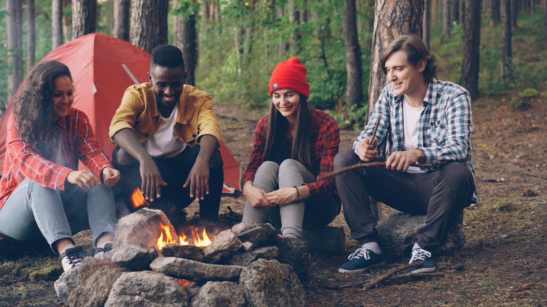 Friends sitting around a bonfire by a tent in the woods