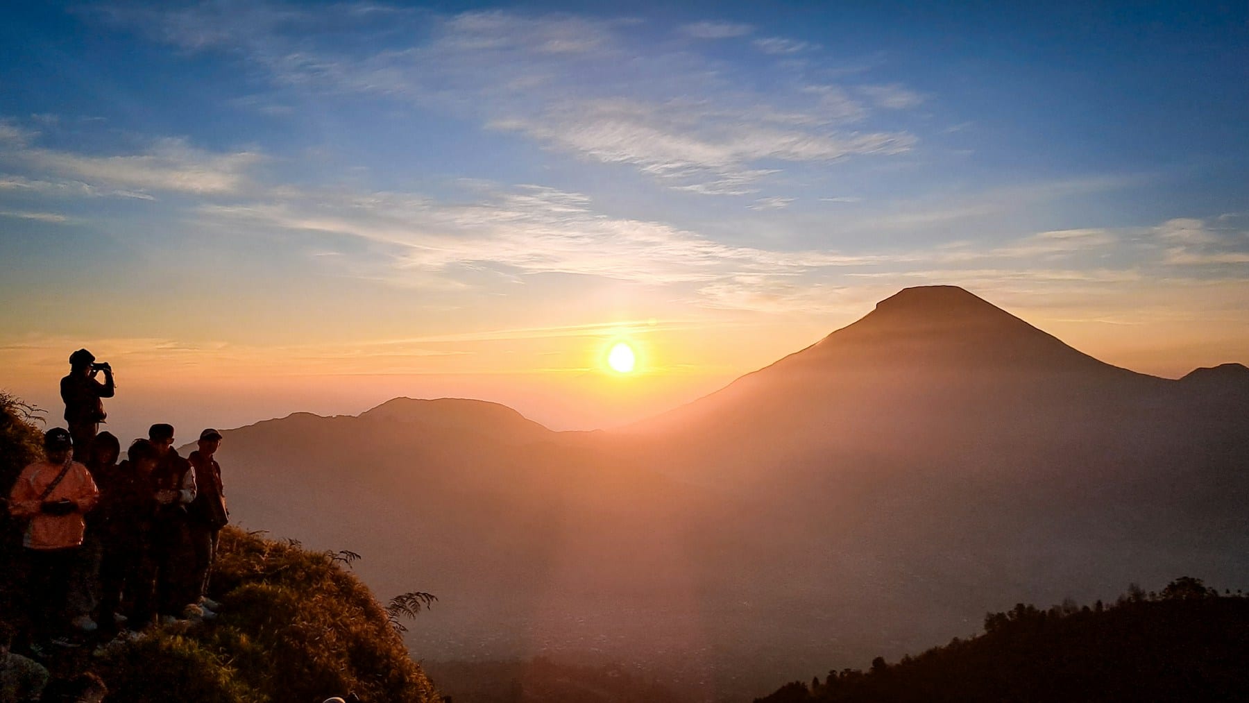Group of hikers silhouetted against a sunrise on a misty ridge